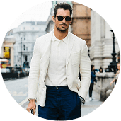 Man in white blazer and sunglasses walking in city.