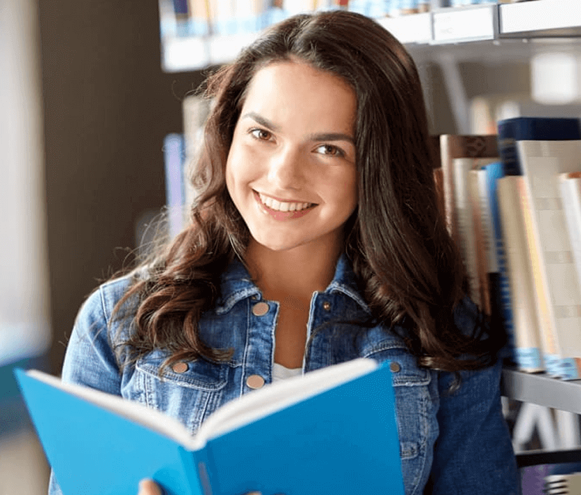 Smiling young woman reading a blue book in a library.